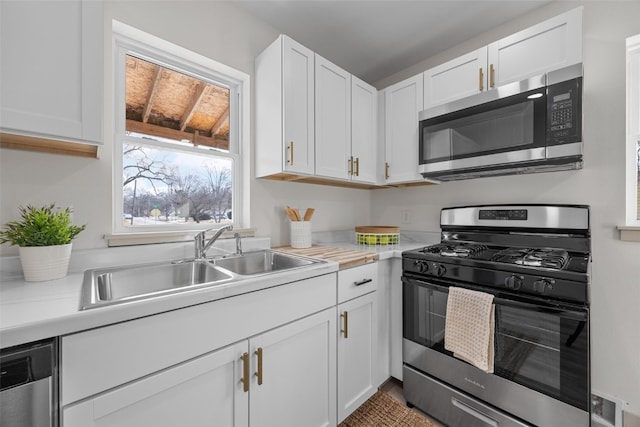 kitchen featuring stainless steel appliances, light countertops, a sink, and white cabinetry