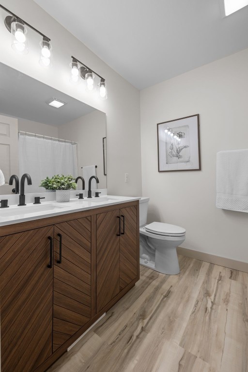 bathroom with double vanity, wood finished floors, a sink, and toilet