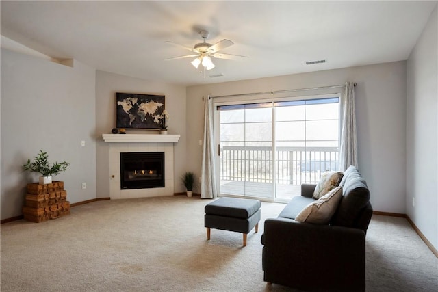 carpeted living area featuring ceiling fan, a tiled fireplace, visible vents, and baseboards