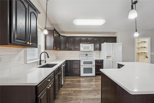 kitchen with white appliances, dark wood-type flooring, hanging light fixtures, light countertops, and a sink