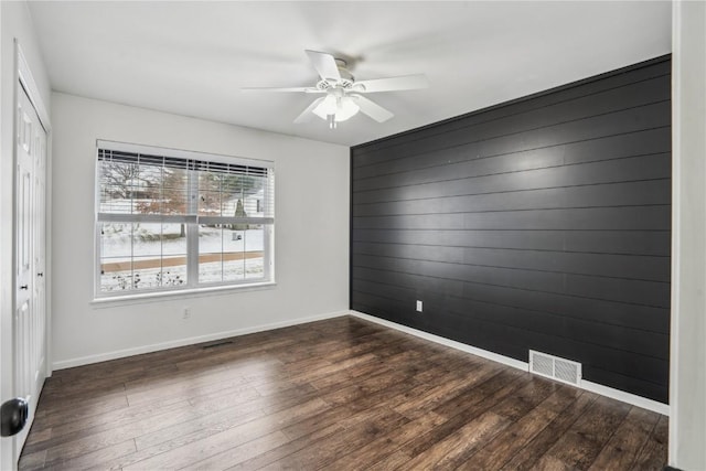 spare room featuring wooden walls, dark wood-type flooring, visible vents, and baseboards