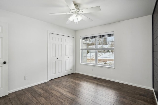 unfurnished bedroom with a ceiling fan, a closet, baseboards, and dark wood-type flooring