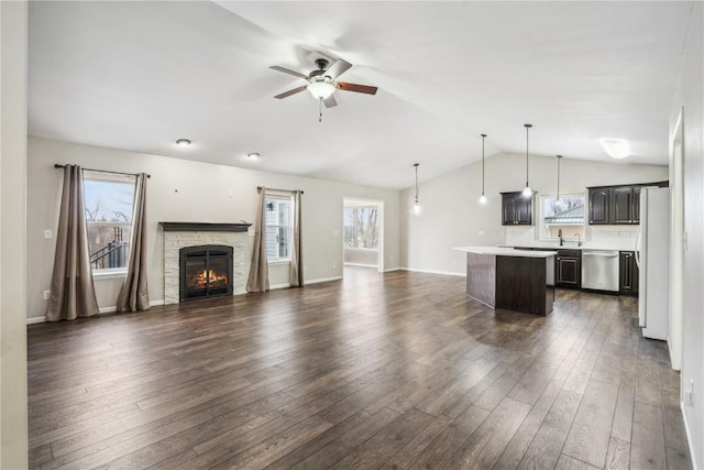 unfurnished living room with a fireplace, lofted ceiling, dark wood-type flooring, ceiling fan, and baseboards