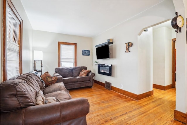 living area with light wood-style floors, baseboards, arched walkways, and a glass covered fireplace