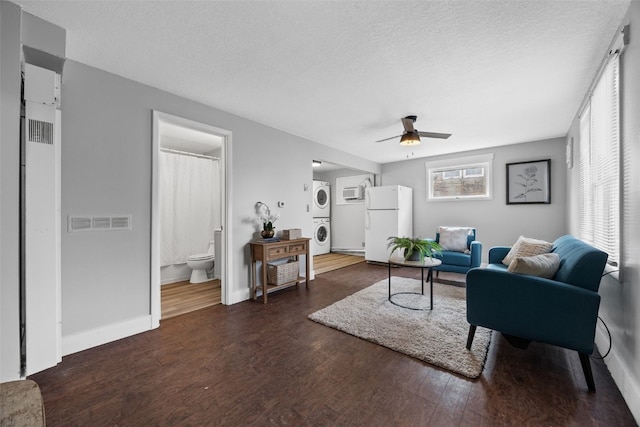 living area with visible vents, ceiling fan, dark wood-type flooring, a textured ceiling, and stacked washing maching and dryer