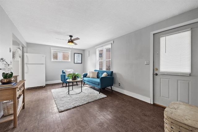 living room featuring a ceiling fan, a textured ceiling, baseboards, and dark wood-style flooring