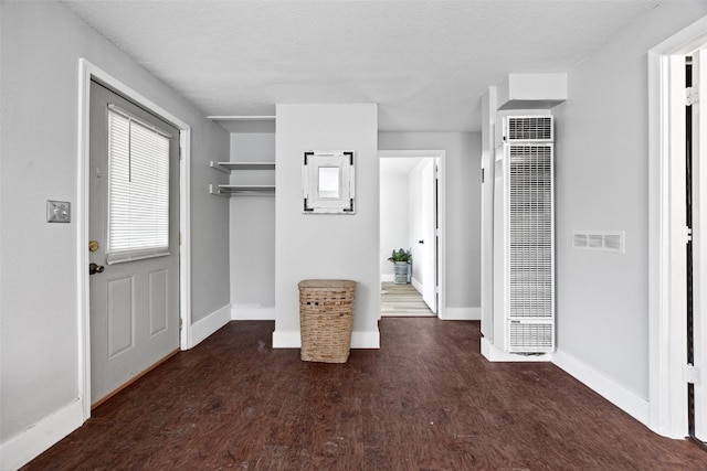 foyer featuring dark wood-style flooring, visible vents, a heating unit, a textured ceiling, and baseboards