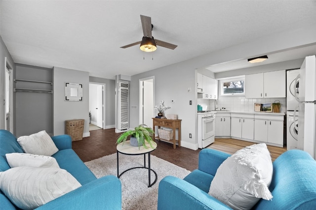 living area featuring ceiling fan, wood finished floors, stacked washer and clothes dryer, and baseboards