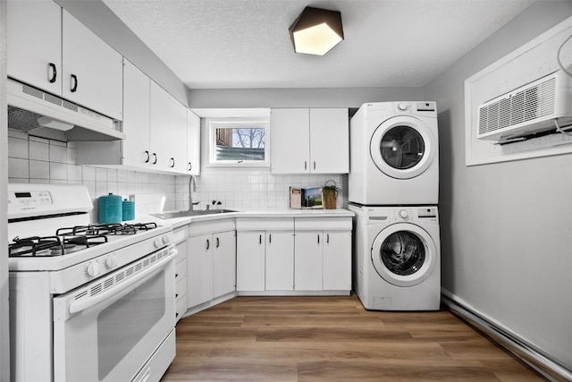 kitchen featuring white range with gas stovetop, white cabinets, stacked washer / drying machine, under cabinet range hood, and a sink