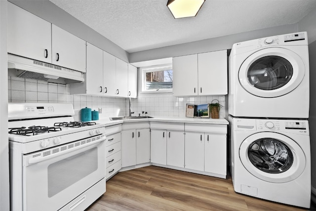 kitchen with stacked washer and clothes dryer, white gas range, light countertops, white cabinetry, and under cabinet range hood