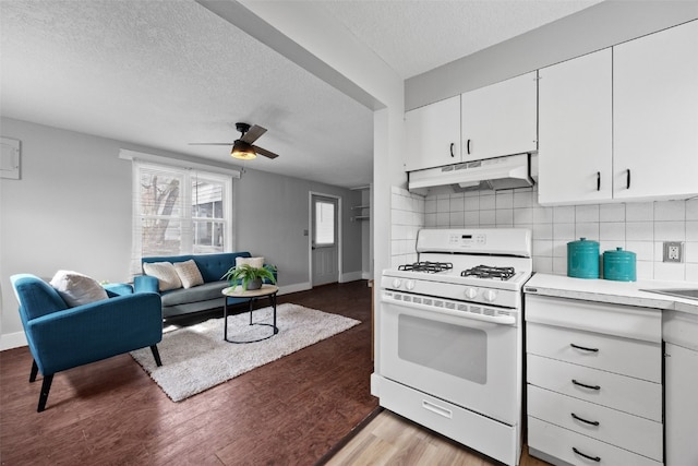 kitchen with white range with gas stovetop, under cabinet range hood, white cabinets, light countertops, and light wood finished floors