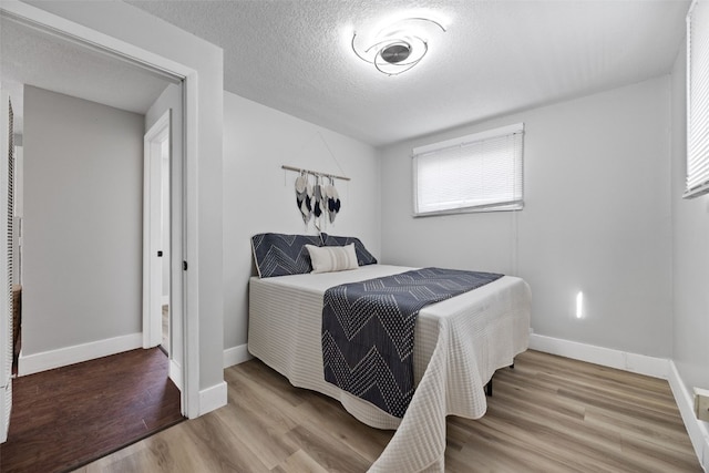 bedroom with a textured ceiling, light wood-style flooring, and baseboards