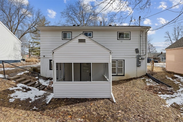 snow covered rear of property featuring a sunroom