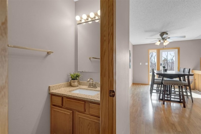 bathroom featuring ceiling fan, a textured ceiling, vanity, wood finished floors, and baseboards