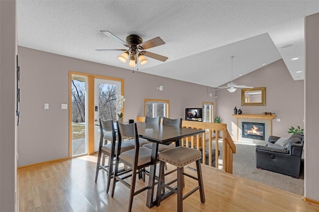 dining space featuring a glass covered fireplace, ceiling fan, vaulted ceiling, a textured ceiling, and light wood-style floors