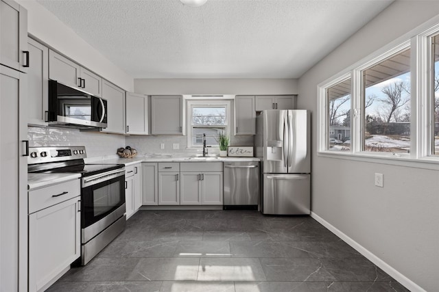 kitchen featuring stainless steel appliances, a sink, baseboards, light countertops, and tasteful backsplash