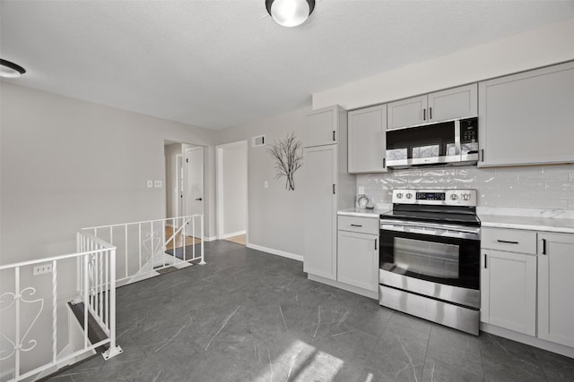 kitchen featuring tasteful backsplash, gray cabinets, a textured ceiling, stainless steel appliances, and light countertops