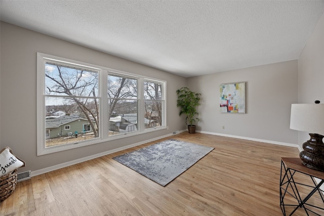 living area featuring a textured ceiling, light wood finished floors, and baseboards