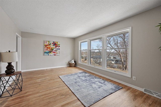 living area with baseboards, a textured ceiling, visible vents, and wood finished floors