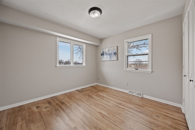 unfurnished bedroom featuring light wood-style flooring, multiple windows, visible vents, and baseboards