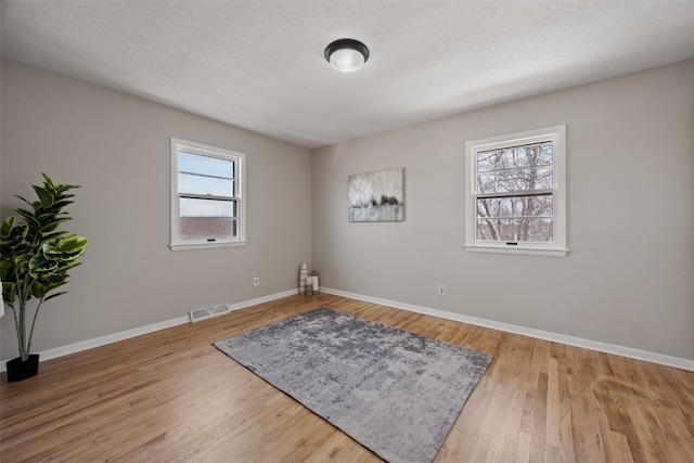 unfurnished room with baseboards, a textured ceiling, visible vents, and wood finished floors