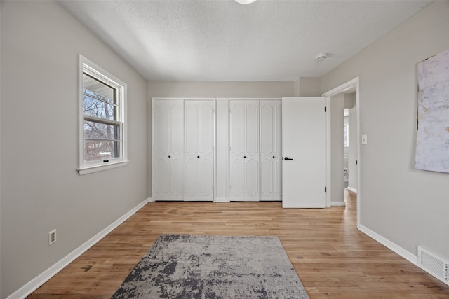 bedroom featuring baseboards, visible vents, a textured ceiling, and light wood finished floors