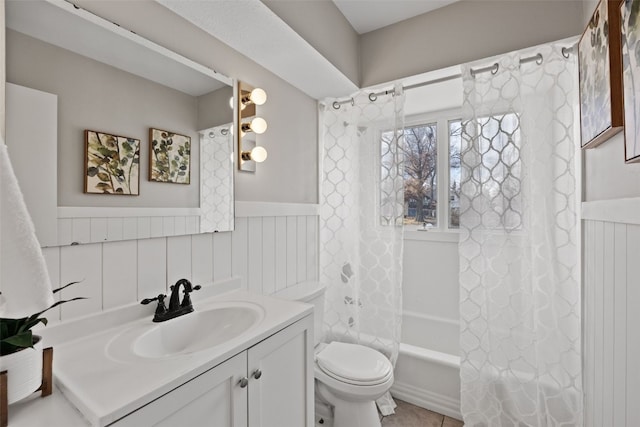 bathroom featuring toilet, vanity, shower / tub combo with curtain, and wainscoting