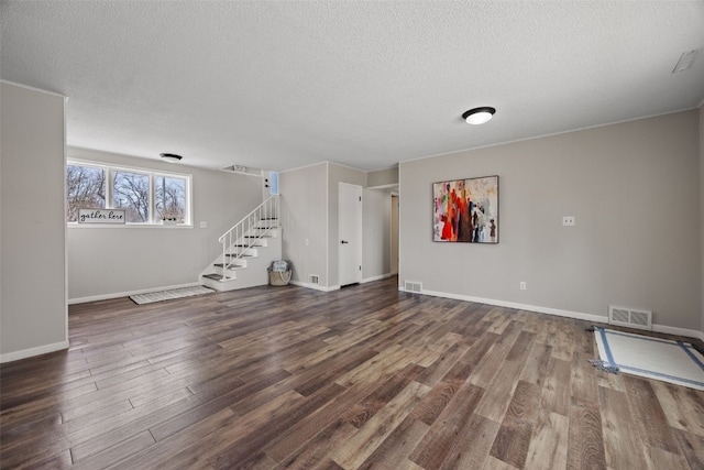 interior space with a textured ceiling, wood finished floors, visible vents, baseboards, and stairs