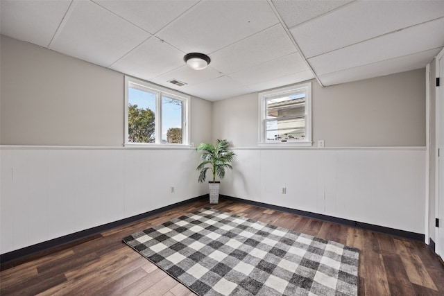 spare room with a paneled ceiling, dark wood-style flooring, plenty of natural light, and visible vents