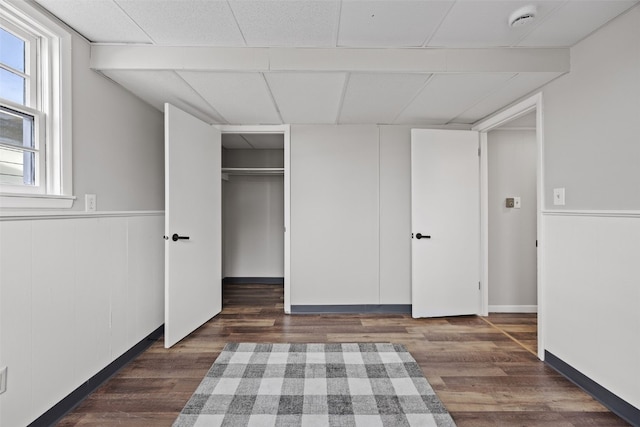 unfurnished bedroom featuring dark wood-style floors, wainscoting, a drop ceiling, and a closet