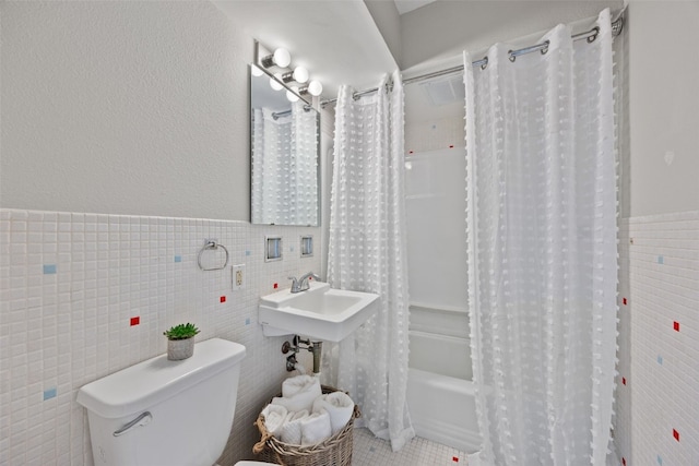 bathroom featuring tile walls, shower / bathtub combination with curtain, toilet, wainscoting, and a sink