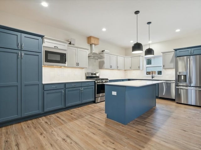 kitchen featuring light countertops, appliances with stainless steel finishes, white cabinetry, a kitchen island, and wall chimney range hood