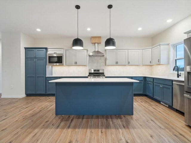 kitchen featuring stainless steel appliances, white cabinets, light countertops, wall chimney range hood, and hanging light fixtures