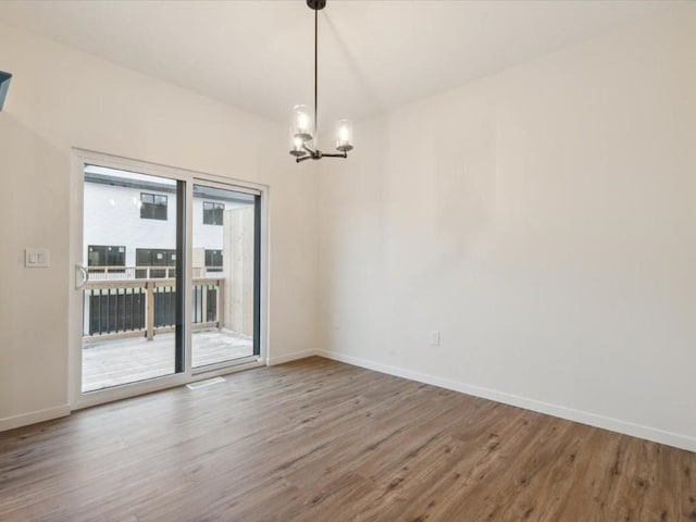 spare room with a notable chandelier, baseboards, and wood finished floors