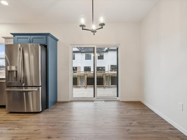 unfurnished dining area featuring baseboards, a notable chandelier, and light wood-style floors