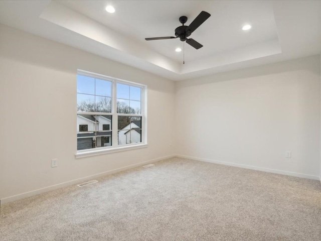 carpeted spare room with visible vents, baseboards, a raised ceiling, and recessed lighting