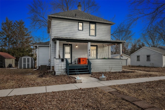 view of front facade featuring a porch, an outbuilding, roof with shingles, and a storage unit