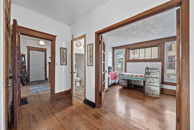 hall featuring dark wood-style floors, baseboards, and crown molding