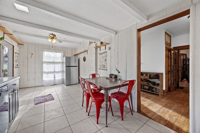 dining room featuring beam ceiling, light tile patterned flooring, ceiling fan, wooden walls, and a textured ceiling