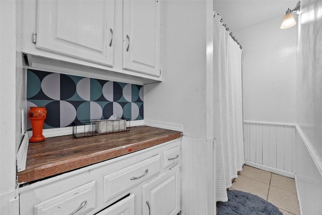 interior space with a wainscoted wall, light tile patterned floors, dark countertops, and white cabinets