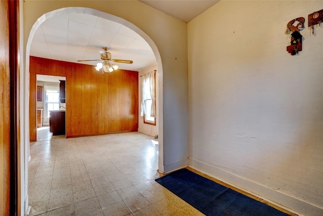 empty room featuring wood walls, plenty of natural light, arched walkways, and tile patterned floors