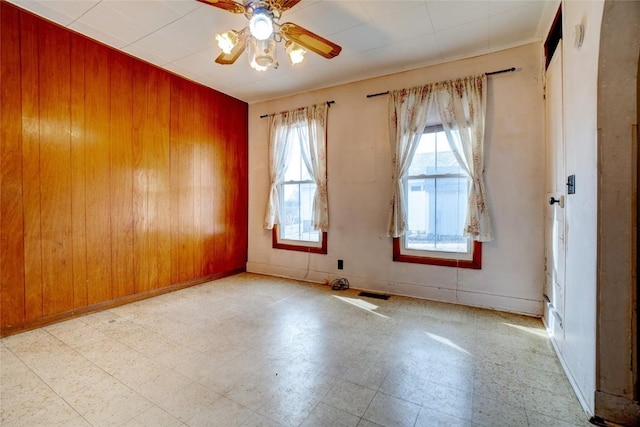 spare room with visible vents, a ceiling fan, wood walls, baseboards, and tile patterned floors