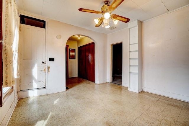 unfurnished room featuring arched walkways, tile patterned floors, a ceiling fan, and baseboards