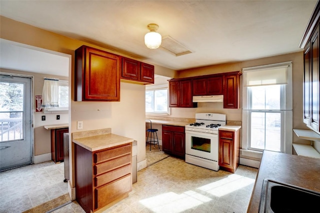 kitchen with reddish brown cabinets, light countertops, white range with gas cooktop, and under cabinet range hood