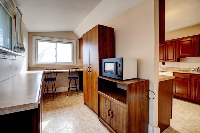 kitchen featuring vaulted ceiling, light floors, dark brown cabinets, and a sink