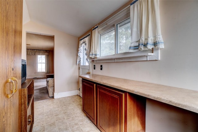 interior space featuring lofted ceiling, a fireplace with raised hearth, light countertops, and baseboards