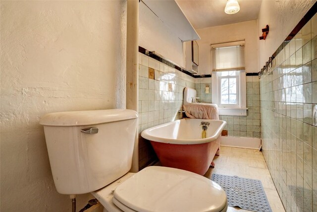 bathroom featuring toilet, a freestanding bath, tile walls, and a textured wall