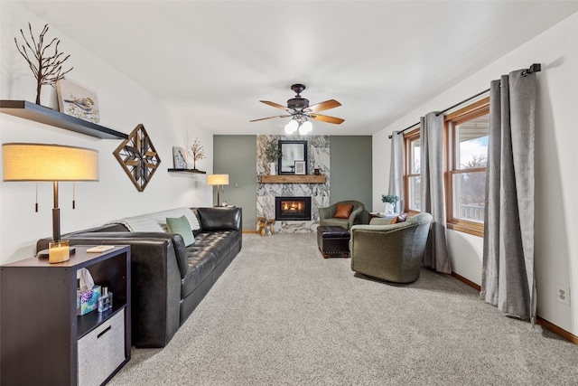 living area with ceiling fan, baseboards, carpet flooring, and a stone fireplace