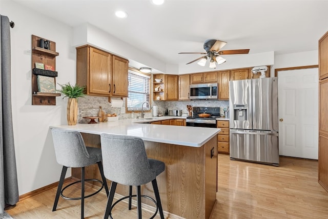 kitchen with decorative backsplash, appliances with stainless steel finishes, light wood-style floors, a peninsula, and a kitchen breakfast bar