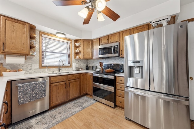 kitchen with a sink, appliances with stainless steel finishes, open shelves, light wood finished floors, and brown cabinetry